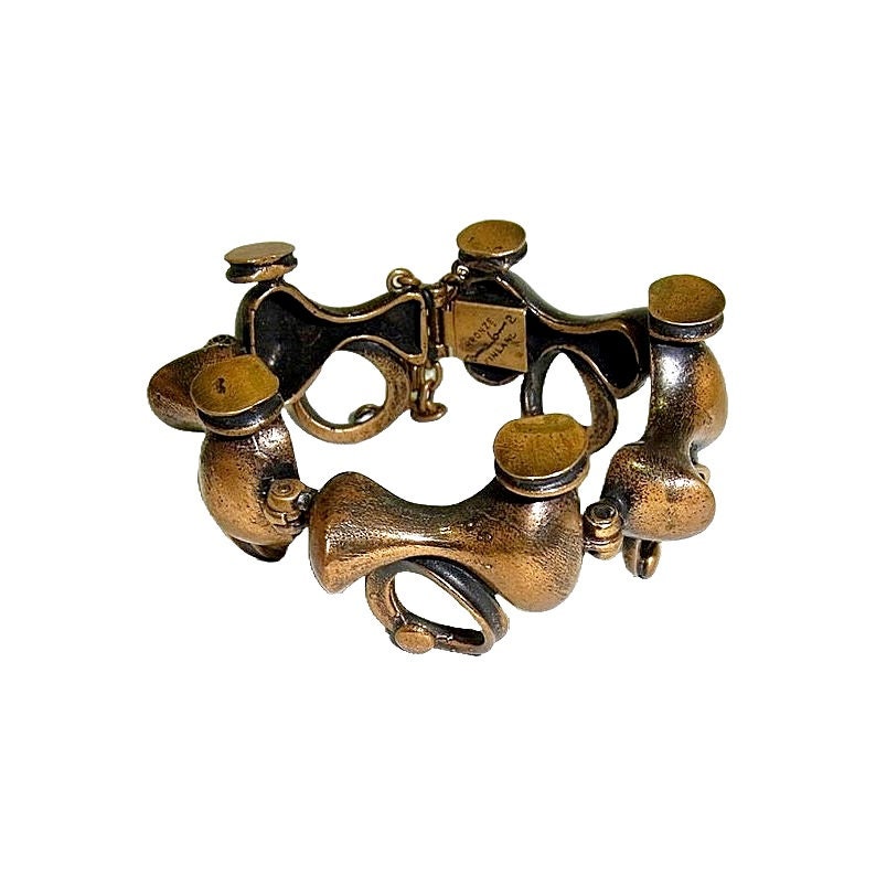 May include: A gold-toned metal bracelet with a unique, abstract design. The bracelet is made up of several interconnected pieces, each with a different shape and texture. The bracelet is marked with the text "BRODY" and "MADE IN USA".