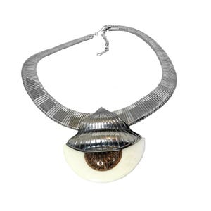 May include: A silver chain necklace with a large, white, shell-shaped pendant. The pendant has a copper-colored center.
