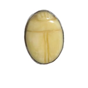 May include: A silver ring with a carved scarab beetle design. The beetle is made of a light yellow material and is set in a silver bezel.