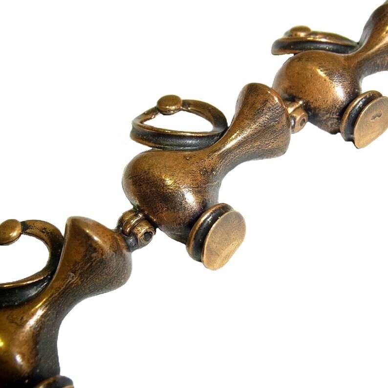May include: A close-up of a bronze chain made of linked, stylized, abstract figures. Each figure has a rounded, bulbous shape with a small, circular handle.
