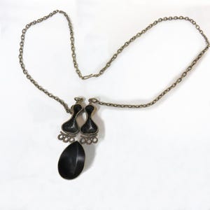 May include: A silver chain necklace with a black pendant featuring two teardrop shapes and a single larger teardrop shape.