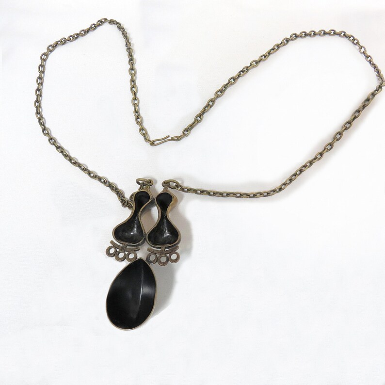 May include: A silver chain necklace with a black pendant featuring two teardrop shapes and a single larger teardrop shape.