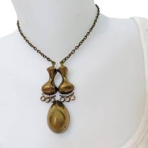 May include: A gold-toned necklace with a pendant featuring two teardrop-shaped charms and a larger teardrop-shaped charm hanging below.