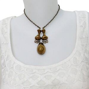 May include: A gold-toned necklace with a unique pendant featuring two teardrop-shaped pieces connected by a smaller teardrop. The pendant has a textured, organic look.