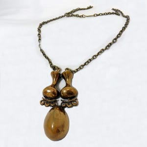 May include: A gold-toned necklace with a pendant featuring two teardrop-shaped charms and a larger oval-shaped charm.