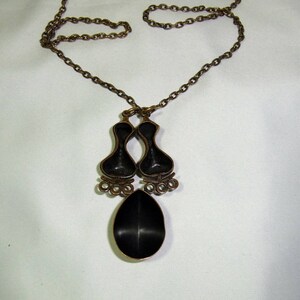 May include: A bronze necklace with a pendant featuring two black enamel teardrop shapes and a single larger teardrop shape. The chain is a simple link style.