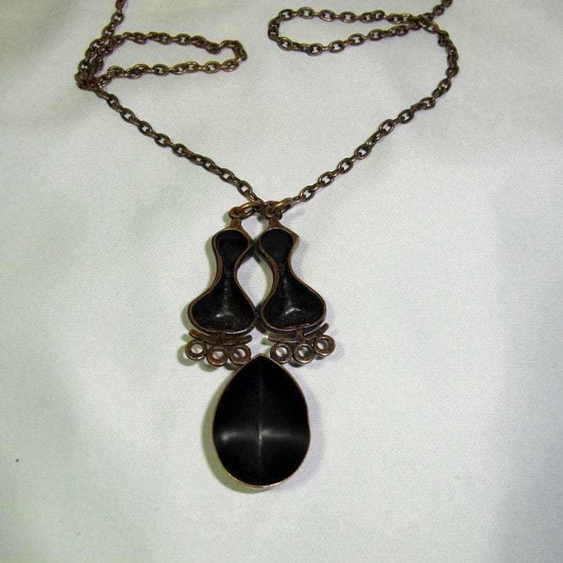 May include: A bronze necklace with a pendant featuring two black enamel teardrop shapes and a single larger teardrop shape. The chain is a simple link style.