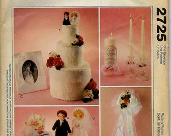 May include: A wedding themed craft pattern featuring a three-tiered cake, a bride and groom doll, a tissue box cover, and a candle holder. The pattern is titled "2725 One Envelope, Une Pochette, Un Sobre".