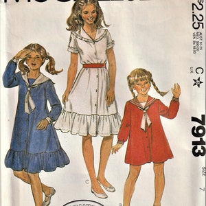 May include: A vintage sewing pattern for three girls' dresses. The pattern is for sizes 7, 8, 10, 12, and 14. The dresses are all different styles, one is a white dress with a red belt, one is a blue dress with a white collar, and one is a red dress with a white collar. The pattern is from McCall's and is called "Laura Ashley".