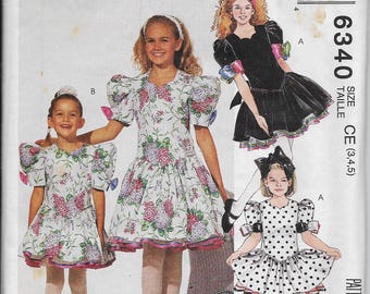 May include: McCall's sewing pattern featuring three girls' dresses. One dress is white with a floral print, another is black, and the third is white with black polka dots. The pattern includes the "Nannette" brand.