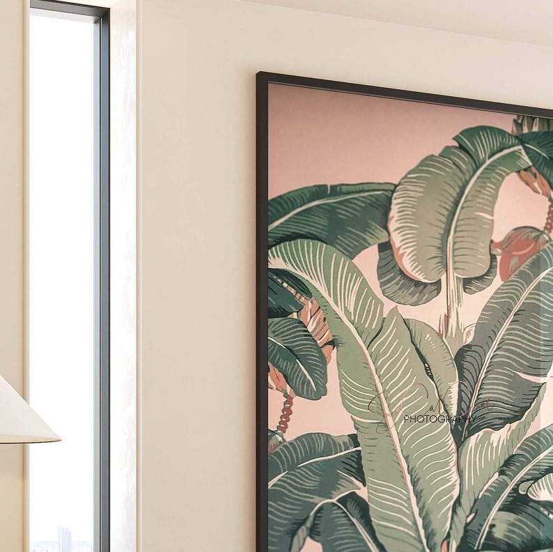 May include: Framed botanical print featuring large green banana leaves with white veining against a soft pink background. The artwork is enclosed in a black frame and includes the word "PHOTOGRAPHY" in the lower right corner.