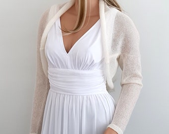 May include: A white knitted shrug with long sleeves. The shrug is made of a lightweight, airy fabric and has a delicate, open-weave design.