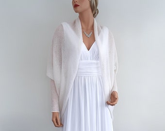 May include: White knitted shrug with long sleeves and a draped open front. The shrug is made of a soft, lightweight fabric and is perfect for layering over a dress or top.