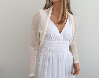 May include: A white knitted shrug with long sleeves. The shrug is made of a lightweight, sheer fabric and has a draped neckline.