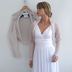 May include: A light beige knitted shrug with long sleeves. The shrug is draped over a white dress form.