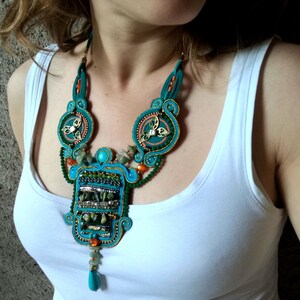 May include: A turquoise and green statement necklace with a large, intricate pendant featuring a geometric design. The pendant is adorned with turquoise and green stones, gold accents, and beads.