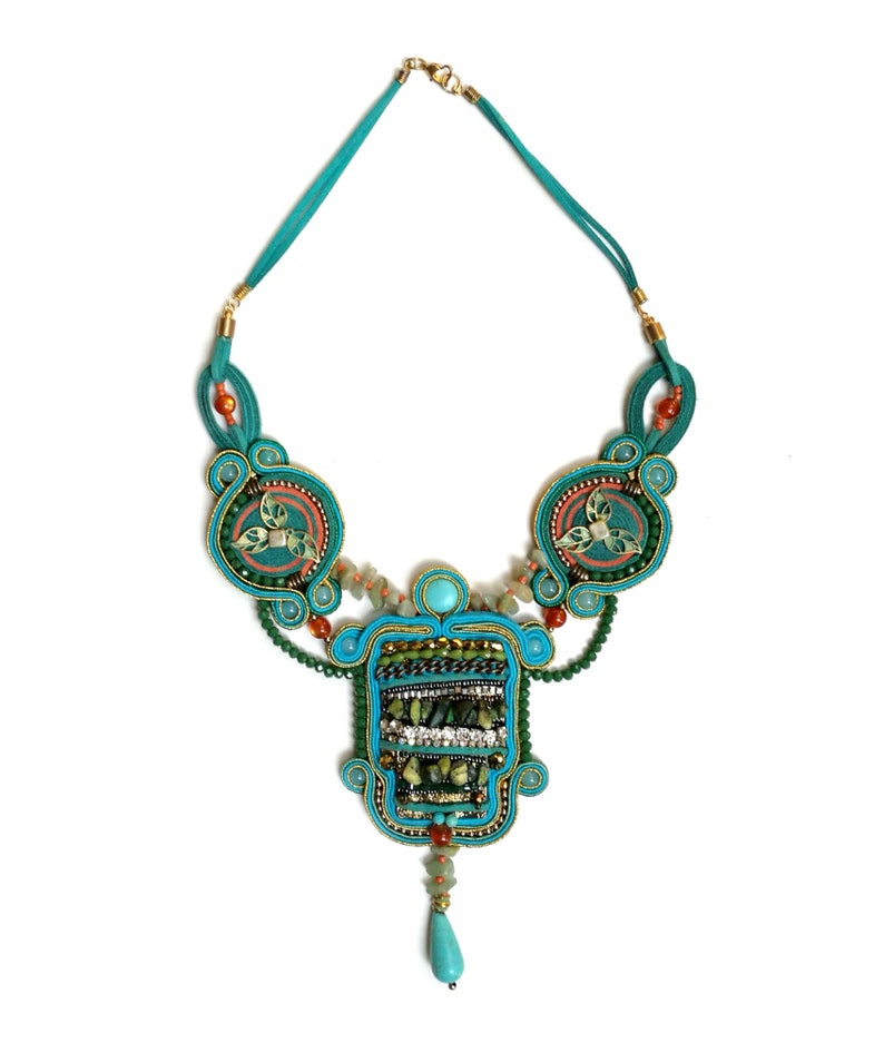 May include: A turquoise and green beaded necklace with a large pendant featuring a geometric design. The pendant is adorned with turquoise, green, and gold beads.