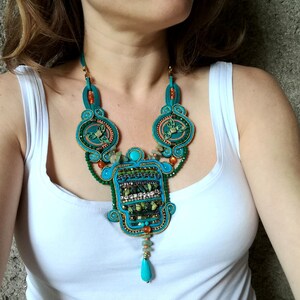 May include: A turquoise, green, and orange statement necklace with a large, intricate pendant. The pendant features a geometric design with beads and crystals.