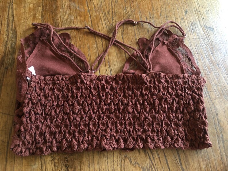 May include: A maroon-colored crop top with a textured, smocked bodice and delicate lace detailing. The top features adjustable spaghetti straps and a soft, layered design. The garment is made of a soft, breathable fabric.