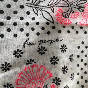 Puede incluir: Tela blanca con lunares negros y dise&ntilde;os florales en negro y rosa ne&oacute;n. Las palabras "free people" est&aacute;n escritas en cursiva. La tela tiene un aspecto ligero y transparente.