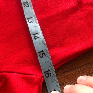 Peut inclure: Un tissu rouge est mesur&eacute; avec un ruban &agrave; mesurer argent&eacute;. Le ruban indique une mesure de 28 &agrave; 40 cm. Le tissu est de couleur rouge vif et uni.