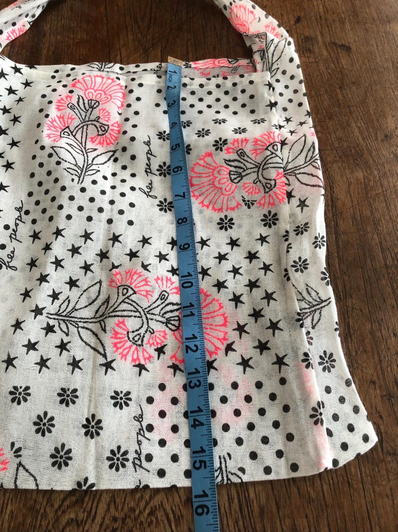 Puede incluir: Bolso tote blanco con un estampado floral y de estrellas. El bolso presenta dise&ntilde;os florales rosas y negros, estrellas negras y lunares negros. El bolso mide aproximadamente 40 cm de largo.