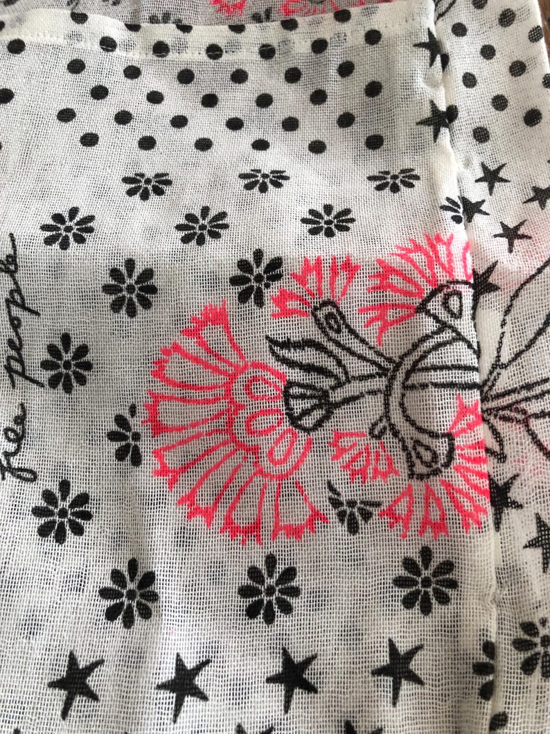 Puede incluir: Primer plano de una tela blanca con un patr&oacute;n repetido de lunares negros, flores y estrellas. Se presenta un gran dise&ntilde;o floral en negro y rosa ne&oacute;n. La palabra "people" est&aacute; escrita en cursiva.