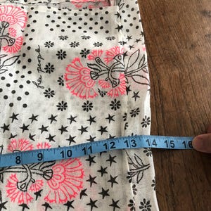 Puede incluir: Tela blanca con un estampado floral y de estrellas. El dise&ntilde;o incluye flores rosas, estrellas negras y lunares negros. Una cinta m&eacute;trica azul muestra un ancho de aproximadamente 20 a 41 cm.