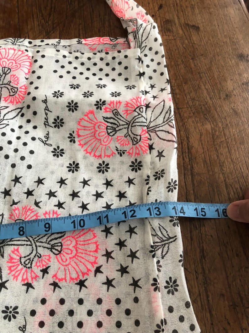 Puede incluir: Tela blanca con un estampado floral y de estrellas. El dise&ntilde;o incluye flores rosas, estrellas negras y lunares negros. Una cinta m&eacute;trica azul muestra un ancho de aproximadamente 20 a 41 cm.