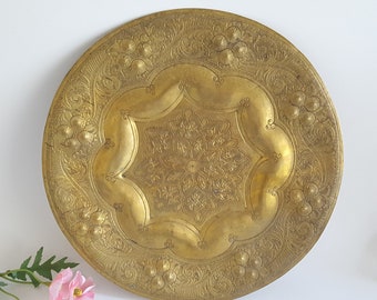 May include: A large, round, gold-colored metal tray with intricate floral and geometric designs. The tray has a raised center with a starburst pattern.