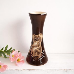 May include: A white ceramic mug with a black handle and the text "But First, Coffee" in a black, bold font. The mug is on a white surface. The mug is approximately 4 inches tall.