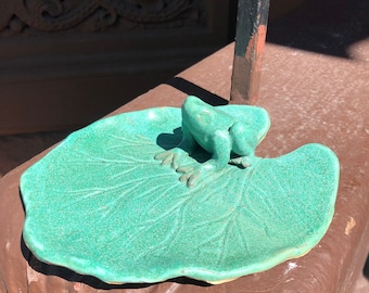 May include: A green ceramic frog figurine sitting on a green ceramic lily pad.