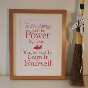 Könnte beinhalten: Ein gerahmter Druck mit weißem Hintergrund und rotem Text, der "You've Always Had The Power My Dear... You Just Had To Learn It Yourself" lautet. Der Druck zeigt ein Paar rote Rubinschuhe.