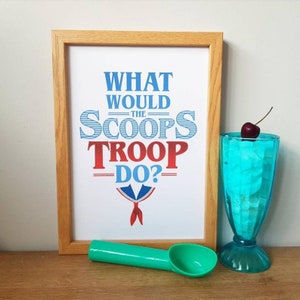 May include: A framed print with the text "What would the Scoops Troop do?" in blue and red lettering. The print features a red and blue sailor collar with a red bow tie. A blue glass with a cherry on top and a green ice cream scoop are also in the image.