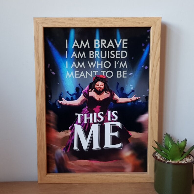 Puede incluir: Una impresi&oacute;n enmarcada de una mujer con un vestido rojo cantando en un escenario. El texto de la impresi&oacute;n dice "I am brave, I am bruised, I am who I'm meant to be, This is me."