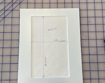 Puede incluir: Cartón de montaje blanco con un marco blanco, marcado con medidas para una imagen de tamaño mediano. Las medidas son 4 3/4 pulgadas por 8 pulgadas.