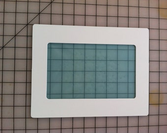 May include: White rectangular frame with a light blue rectangular window inside. The frame is on a grey grid background.