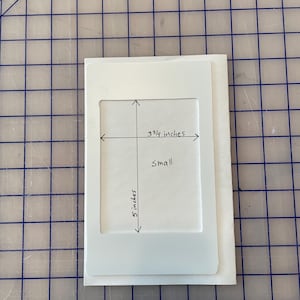 May include: A white cardstock template for a small photo frame, measuring 3 3/4 inches by 5 inches. The template is labeled "Small" and has a white border around the photo opening.