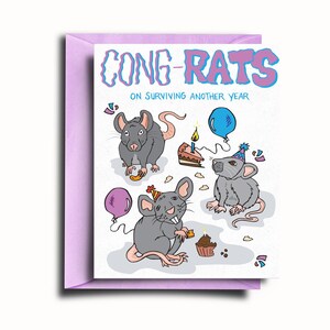 Peut inclure: Une carte d'anniversaire avec un fond blanc et une bordure violette. La carte représente trois rats de dessin animé portant des chapeaux de fête et tenant du gâteau et des ballons. Le texte sur la carte dit "Cong-Rats on surviving another year."