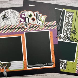 Peut inclure: Une page de scrapbooking noire avec une bordure violette, verte et orange. La page comporte deux espaces pour photos, l'un avec une toile d'araignée blanche et l'autre avec un motif de crâne et d'os croisés. La page a également un titre qui dit "Spooky" en lettres colorées.