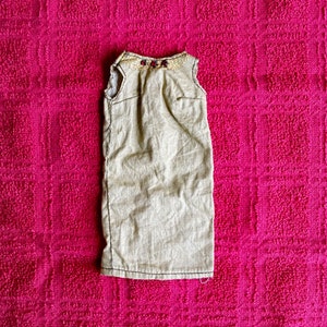 May include: A sleeveless beige dress with a decorative neckline on a pink background.