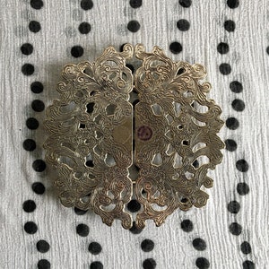 Może przedstawiać: Srebrny metalowy obrączka na serwetkę z ozdobnym, misternym wzorem kwiatowym. Obrączka jest otwarta z obu stron i ma okrągły kształt.