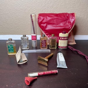 Peut inclure: Une trousse de toilette rouge contenant un ensemble vintage de produits de toilette de voyage, dont une brosse à dents, une lotion capillaire, de l'eau de Cologne, du shampooing, une lotion capillaire, de la poudre dentifrice, de la crème à raser et un rasoir. Le sac a une fermeture à cordon et une poignée en cordon.