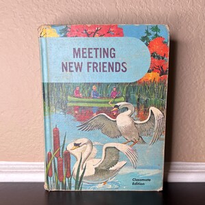 May include: A vintage children's book titled "Meeting New Friends" with a colourful illustration of swans and a canoe on a lake. The book is part of the "Classmate Edition" series.