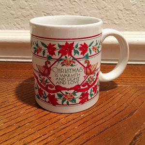Könnte beinhalten: Weiße Keramiktasse mit einem roten und grünen Weihnachtsmotiv. Die Tasse trägt ein Zitat, das lautet: "Weihnachten ist Wärme und Licht und Liebe".
