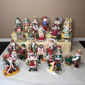 Puede incluir: Una colección de figuras navideñas, con Papá Noel y otros personajes festivos. Las figuras están pintadas con colores vibrantes y varios atuendos, incluyendo rojo, verde y blanco. Algunas figuras sostienen regalos o van en trineos.