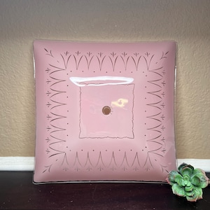 May include: A square, pink glass ceiling light fitting with an etched design around the edges. The light fitting has a white centre with a hole in the middle.