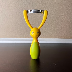 May include: A yellow and green rabbit-shaped vegetable peeler with a stainless steel blade.