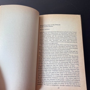 May include: A page from a book titled "Social Functions of the Prisons in the United States" by Bettina Aptheker. The text discusses the use of euphemisms like "correctional facilities" and "inmates" to avoid acknowledging the reality of prisons and the existence of political prisoners in the United States.