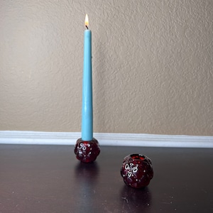 May include: Two red glass candle holders with a textured, berry-like design. One holder has a light blue candle inside.